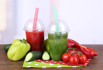 Fresh vegetable juices in plastic cups on wooden table, on light background