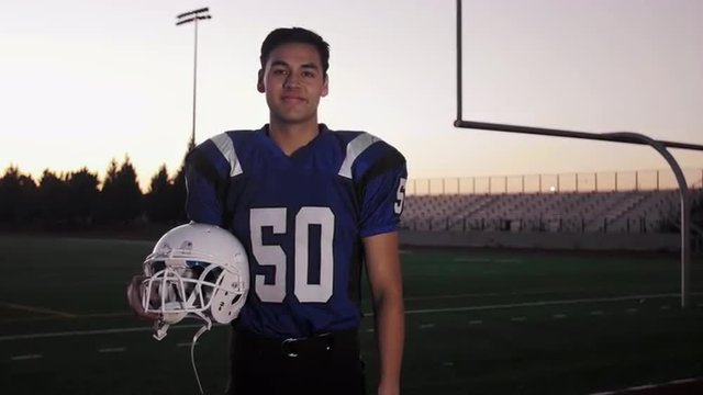 Portrait of a football player on a field holding his helmet
