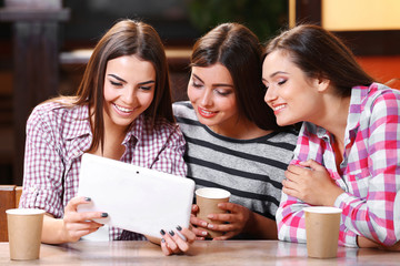 Three smiling friends with coffee looking at tablet