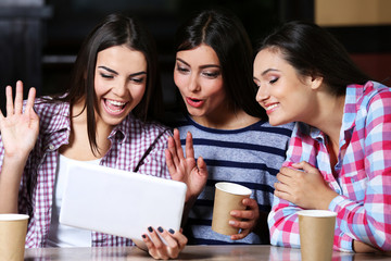 Three smiling friends look in tablet sitting in cafe