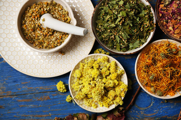 Assortment of dry medicinal herbs in bowls on wooden background top view