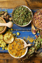 Assortment of dry medicinal herbs in bowls on wooden background top view