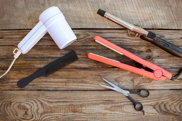 Hair accessories: hair dryer, curling iron, hair iron, comb, scissors on the old wooden background. Toned image  
