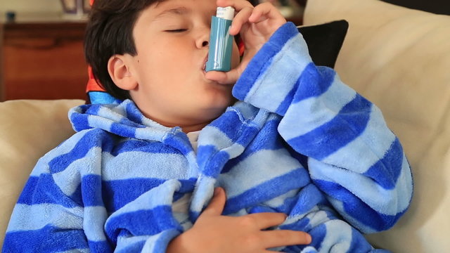 Young boy  seated on a sofa taking asthma treatment with inhaler
