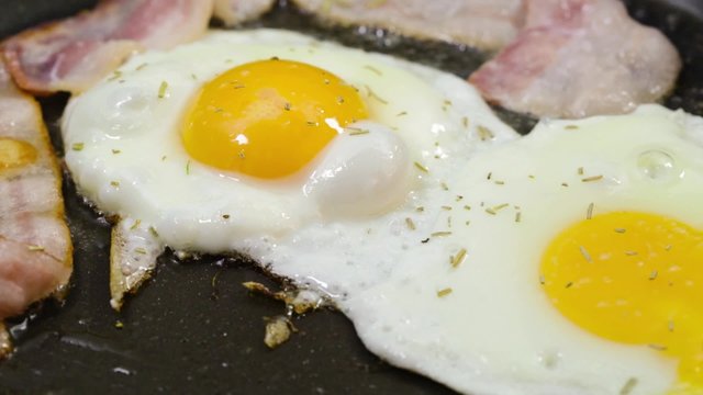 Eggs and Bacon. Three strips of bacon frying in a pan with an egg. 