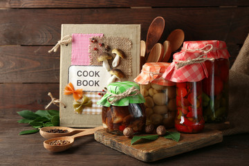 Jars with pickled vegetables and beans on wooden background
