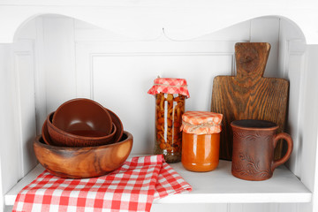 Jars with pickled vegetables and kitchenware on shelf