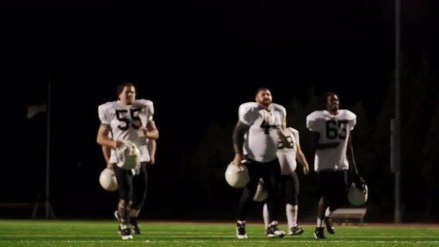 Five football players running onto the field at night
