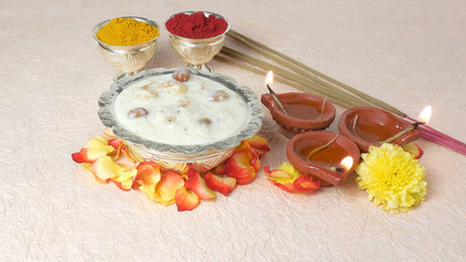 Diwali concept, highlighted through a sweet dish, vermicelli or semiya payasam, earthen lamps and turmeric powder and red pigment in silver cups.