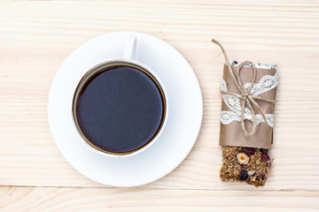 Homemade rustic granola bars with dried fruits and handmade packaged and cup of coffee on wooden background
