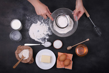 a woman sifts the flour into a bowl and next to it are various ingredients for a dish on a black background