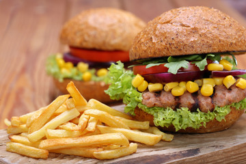 Grilled hamburger with fries tomato onion and corn on wooden bac