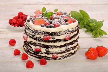 Chocolate cake with white cream and fresh fruits on wooden backg