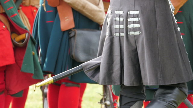 The back of the guard showing his sword. The guard is giving instructions to the others holding his sword on the side