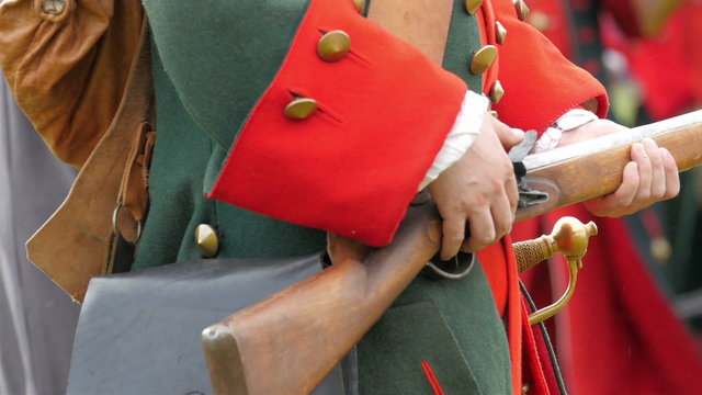 The guard in red uniform holding his gun then putting on the bullet and a powder from his pouch.