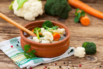 Cooked cauliflower and broccoli in clay bowl with wooden spoon
