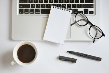 Coffee cup, spiral notebook, computer keyboard, and pen on white