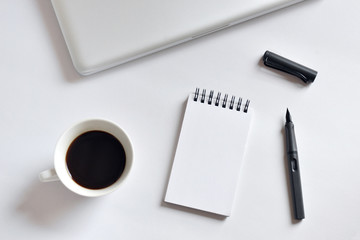 Coffee cup, spiral notebook, laptop, and pen on white background