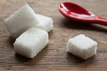 sucre en morceaux et petite cuillère rouge sur fond en bois