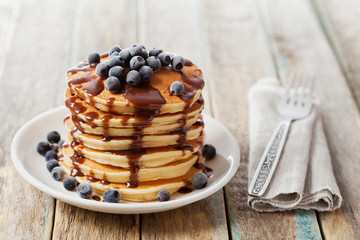 Stack of baked pancakes or fritters with chocolate sauce and frozen blueberries in a white plate on a wooden rustic table, delicious dessert for breakfast