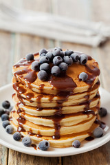 Stack of baked pancakes or fritters with chocolate sauce and frozen blueberries in a white plate on a wooden rustic table, delicious dessert for breakfast