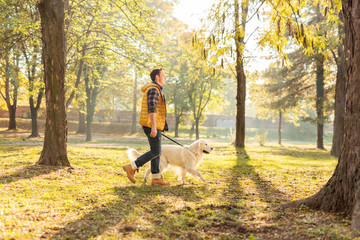 Young man walking his dog in a park - obrazy, fototapety, plakaty