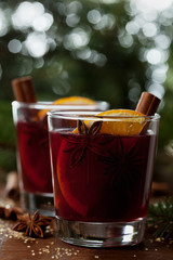 Christmas mulled wine or gluhwein with spices and orange slices on rustic table, traditional drink on winter holiday, magic light, selective focus