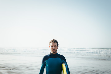 Male surfer beach lifestyle portrait. Man in wetsuit with bodyboard surfing equipment.