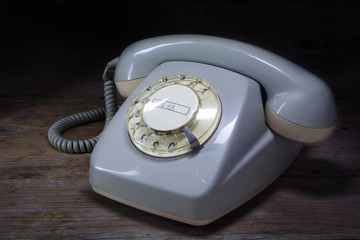 retro rotary telephone of gray plastic with rotary dial on a dar