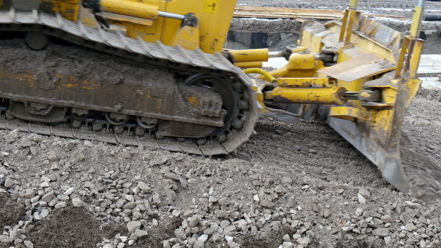 Yellow bulldozer with big tires on a construction. The bulldozer is getting some big stones to flatten the soil