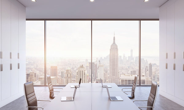 Workplaces or conference area in a bright modern open space office. White tables equipped by modern laptops and black chairs. New York view. 3D rendering. A sunset. Toned image.