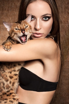 Awesome caucasian attractive sexy fashion model with long brunette natural hair, beautiful eyes, full lips, perfect skin posing  in studio, holding Bengalian cat, beauty photo shoot, retouched image