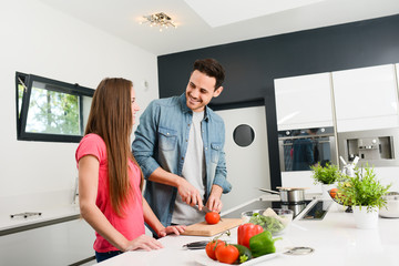 beautiful and happy young couple preparing organic vegetable salad together in kitchen at home