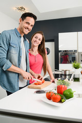 beautiful and happy young couple preparing organic vegetable salad together in kitchen at home