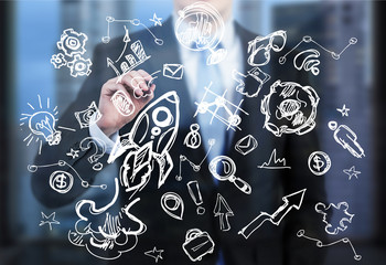 A business person is writing a numerous business icons on the glass screen in the modern panoramic...