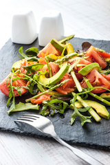 Vegetable salad with trout and asparagus on the black stone with fork vertical