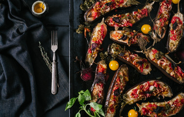 Baked eggplant and vegetables in a black metal pan and vintage fork on a black background of the old wooden boards top view
