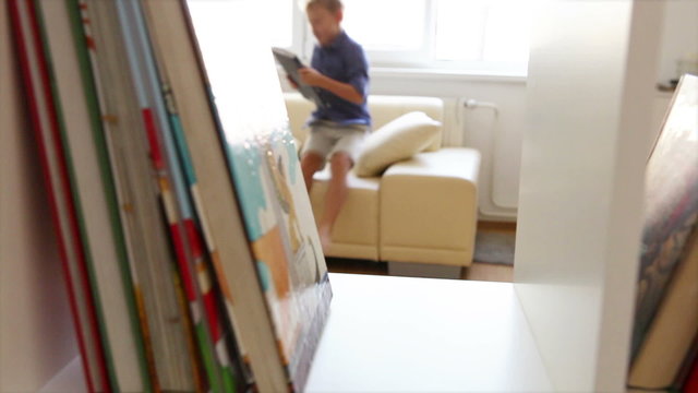 Little boy jumps into cosy sofa with his favorite book