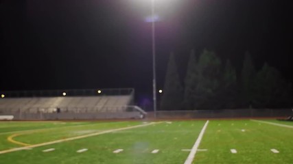 Two football players running a drill on the field at night
