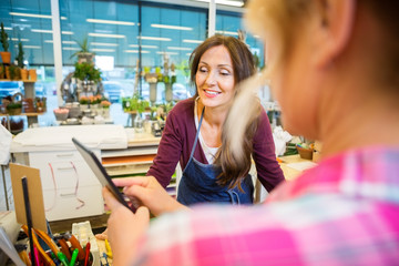 Florist Looking At Female Customer Using Digital Tablet