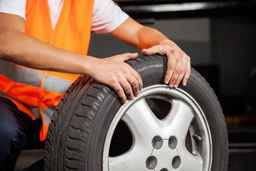 Obraz premium Mechanic With Car Tire At Garage