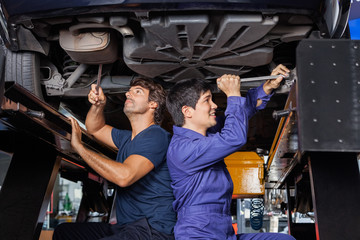 Obraz na płótnie Canvas Mechanics Working Under Lifted Car