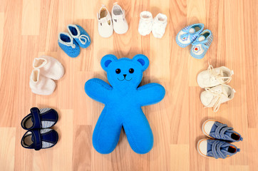 Baby boy shoes arranged on the floor. Tidy tiny child boots nicely arranged and a teddy bear.
