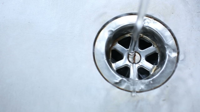 Water pouring into a stainless steel sink and running into the plug