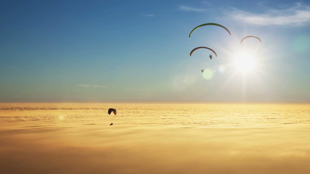 Paragliders on a sea of golden clouds with sun