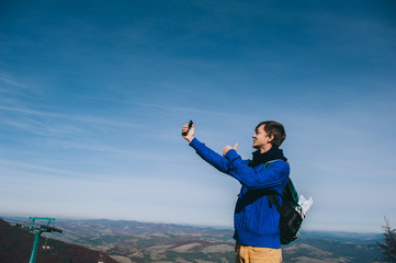 Young hipster taking photo by smart-phone on the peak of mountai