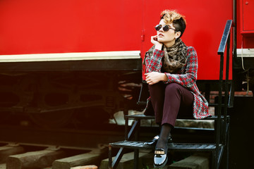 Fototapeta na wymiar Fashion portrait of young beautiful stilish woman with round sunglasses. Lady sitting on stairs of stairway. Bob short hair. City lifestyle. Street fashion concept. Copy space.Toned
