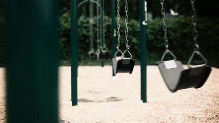 Evil Swings. a long shot of empty swings swaying in the breeze at a playground with a shrub line in the background. evil, creepy feel
