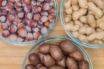 Bowls of raw hazelnuts and pecan nuts on a wooden background. Oleaginous