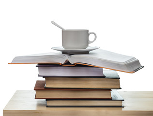 Obraz premium Stack of books and a cup with a spoon on a wooden table isolated on white background.